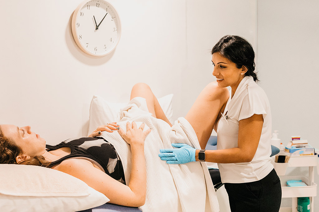 A physiotherapist assessing a pregnant client who is lying on a treatment bed